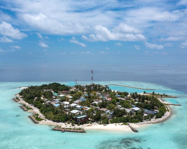 An aerial image of a small island surrounded by light blue water. An aerial image of a small island surrounded by light blue water.